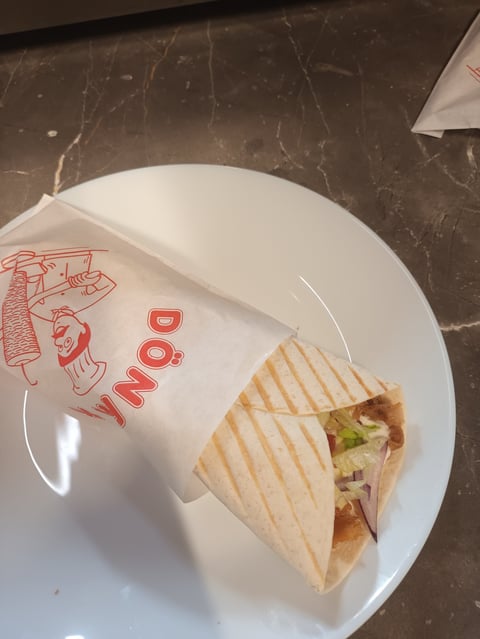 Wrapped sandwich on white plate with red deli branding, placed on dark marble surface