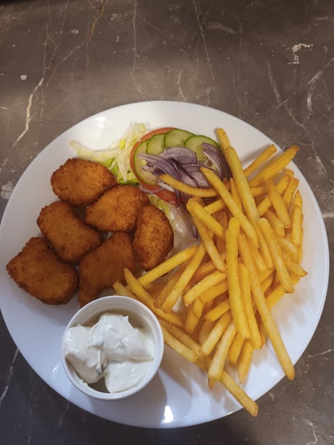 Plate with golden fried chicken nuggets, French fries, sliced onion, lettuce, and white dipping sauce on a textured surface