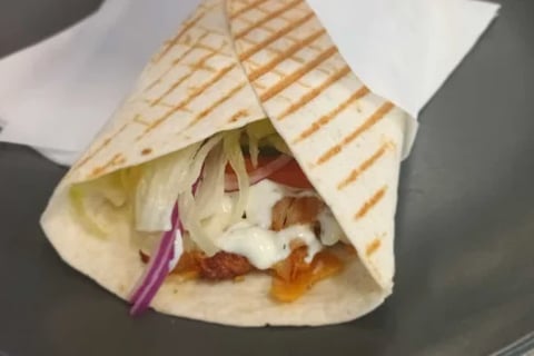 Grilled tortilla wrap filled with meat, sour cream, lettuce, and red onion slices