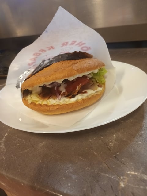 Sandwich with ham, lettuce, and cheese on a toasted bun, wrapped in paper, served on a white plate