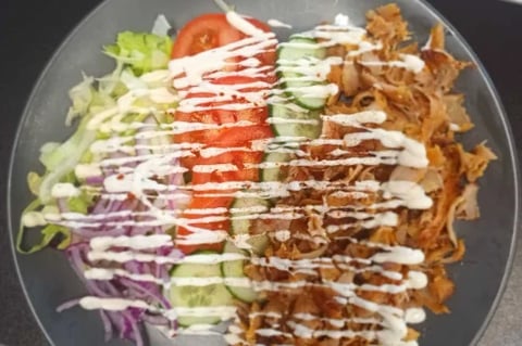 Overhead view of a plated salad with lettuce, tomato, cucumber, shredded cabbage, fried onions, and creamy drizzle sauce
